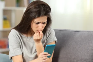 A young woman sitting on the couch staring at her phone, she just posted a sadfishing post on social media