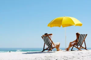 A couple sits on the beach under a yellow umbrella. Summer vacations can't fix all marriage problems, but you can use the optimism of summer to address deeper issues.
