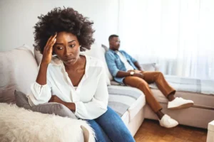 A woman sits on a couch on the other end from her husband, with whom she is clearly angry. Imagine they hit one of your “buttons,” and you had an angry outburst at your spouse. How do you repair the relationship?