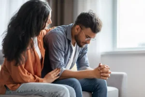 A woman sits on a couch with her husband, comforting him after and argument. Don't let your spouse make you angry. When you feel strong emotion (a reaction), slow down and decide what to do next (a response).