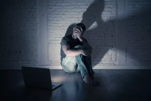 A man hides his face in shame from a computer screen in a dark room. People may use sex and pornography to activate a “pleasure system high” that can lead to a deeper progression of pornography addiction.