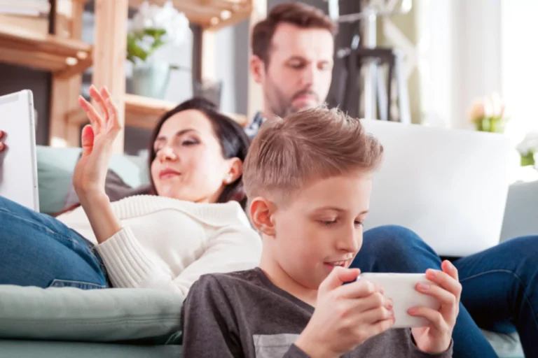 Family sitting on a couch, each absorbed in their own devices, highlighting the need for a screen time reset.