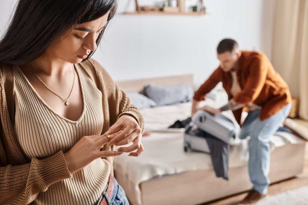 A woman takes off her wedding ring in the foreground, as her husband packs his suitcase in the background. Here are three grains of truth to help you thrive when your spouse wants a separation or divorce.