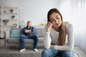 A woman sits across the room in front of her husband, sad with her head on her hand. Recognizing when unmet expectations are the source of anger in your marriage can help you can create an environment for reconciliation.