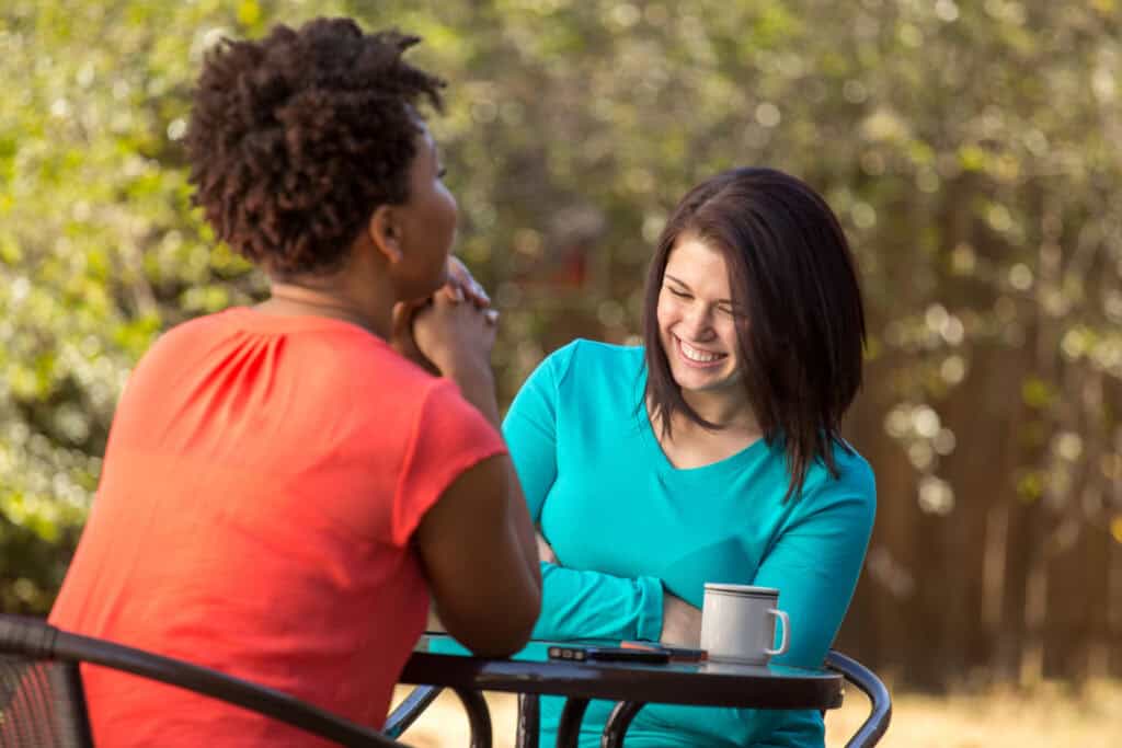 Two women sitting at an outdoor table and talking.