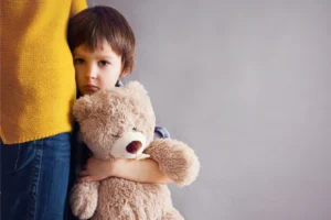 little boy holding a large Teddy bear leaning against his mom