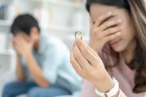 A woman holds her wedding ring in shame, while her husband, slightly out of focus, sits on the other end of the room sadly holding his head in his hands. If you recently discovered your spouse has been unfaithful, I want to offer some guidance on how to recover from marriage infidelity.