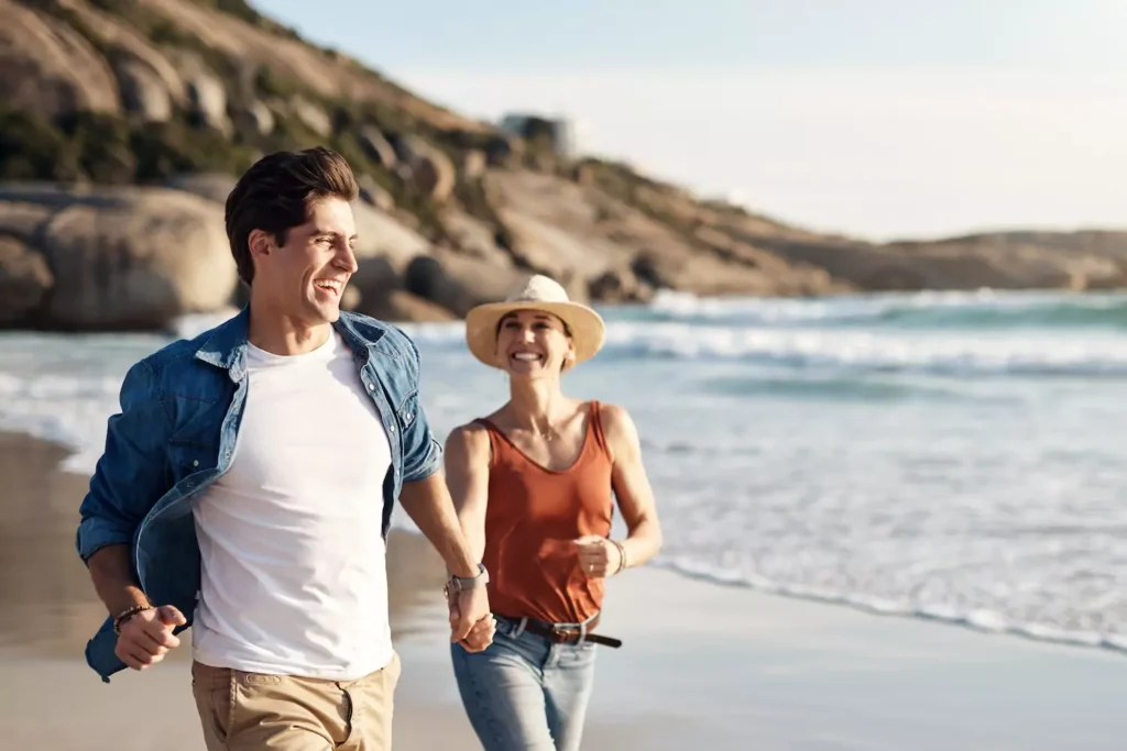 A man and his wife joyfully run hand-in-hand-down a shoreline with big smiles on their faces. Here are five ways to cultivate more consistent joy in your marriage as you strive to reflect Christ's joy in your love for your spouse.