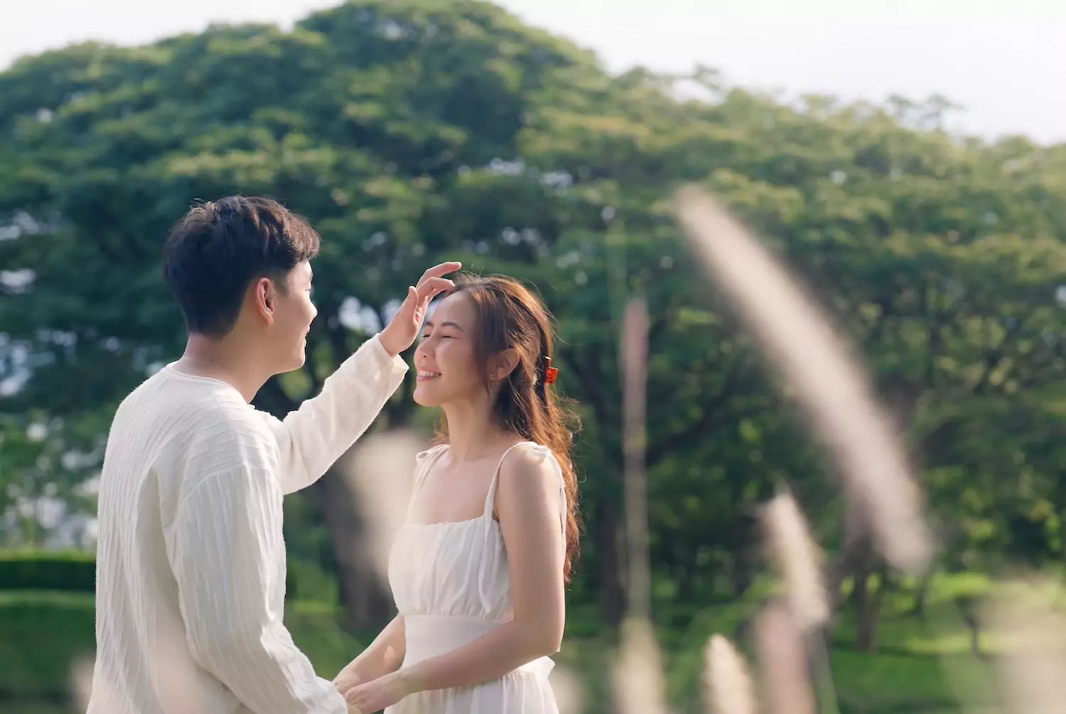 A young married couple gaze longingly at each other in a field with some trees in the background. The newlywed wife holds her husband's right hand, as he lovingly strokes here hair. Can romantic love be reconciled with unconditional commitment in marriage? Yes. Covenantal commitment helps romantic love fulfill itself.