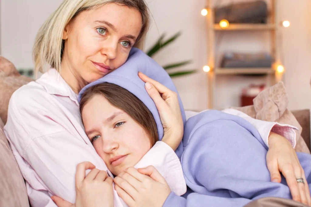 An image depicting mother and teenage daughter sitting closely together on a couch.