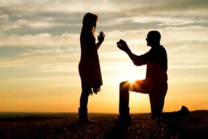 A young man on one knee proposes to a girl at sunset.