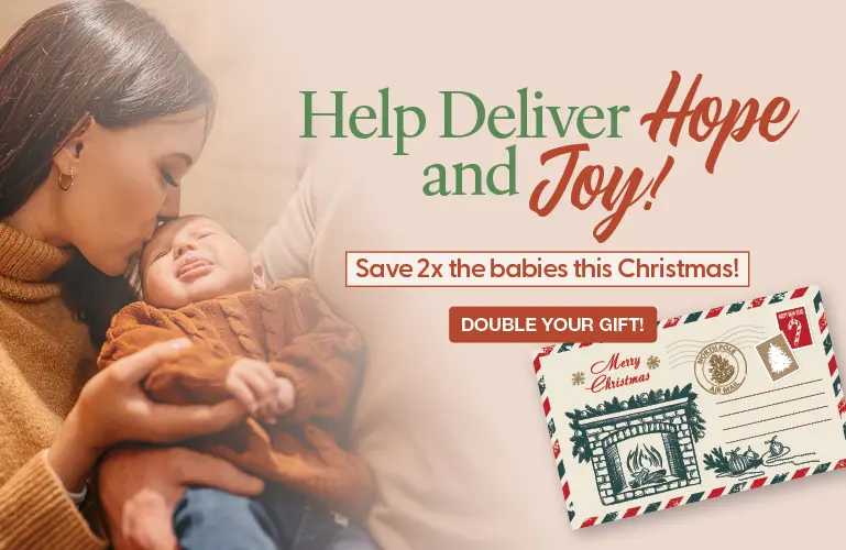 A loving mother holding her infant during the holiday season, inviting donors to double their gift and save more babies this Christmas.