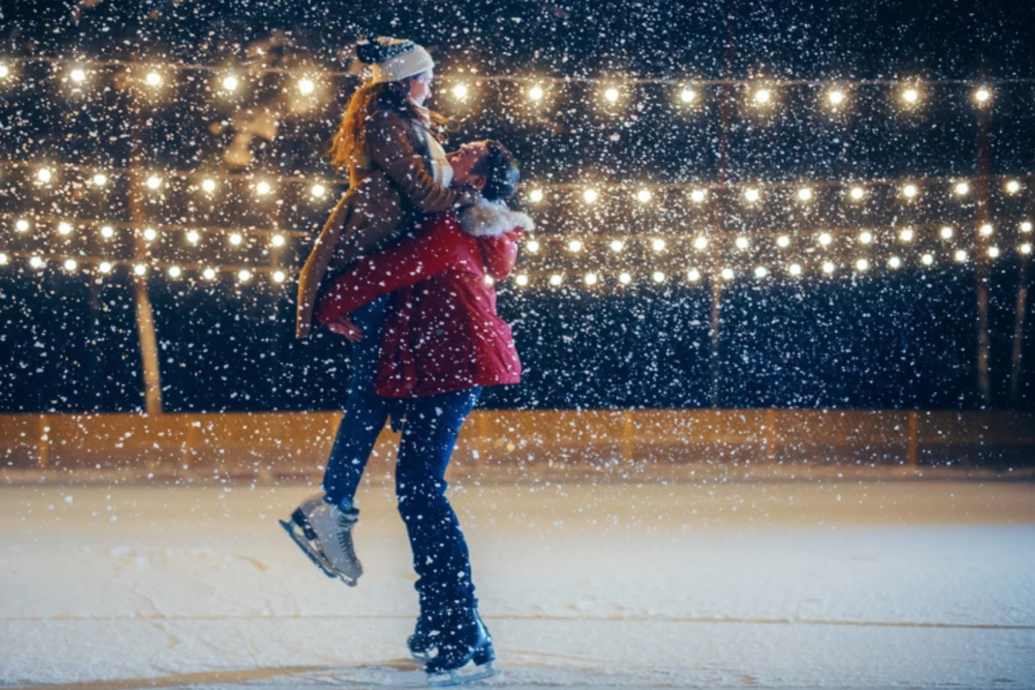 Couple ice skating on a snowy winter night by the light of strings of Christmas lights