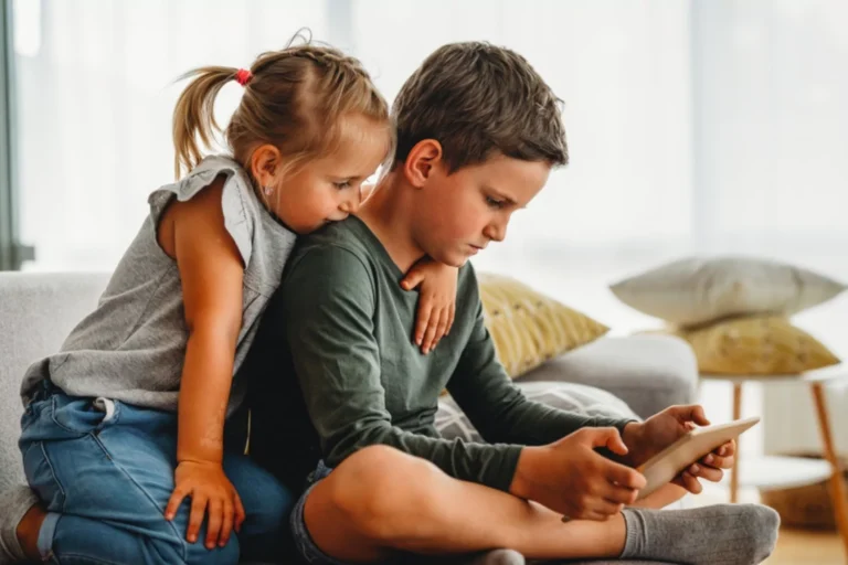 A young boy watching a tablet closely while a younger girl leans over his shoulder, illustrating the immersive nature of screen time and its potential TikTok effects on kids.