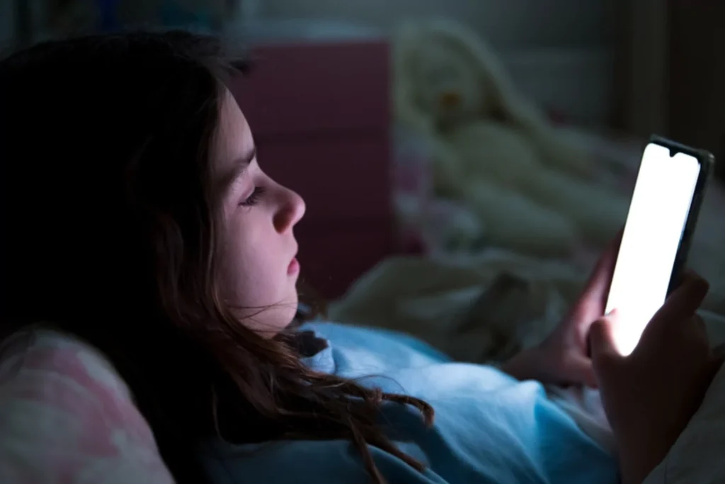 young teen laying dow in the dark looking at her phone