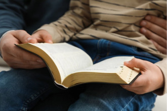 A parent and child sitting together, reading a Bible, focusing on spiritual growth and sharing faith.