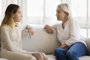 A mother and her preteen daughter sit on a couch in a bright living room, engaged in a thoughtful conversation. This image represents how to talk to preteens about sex in an open and supportive way, fostering trust and communication.