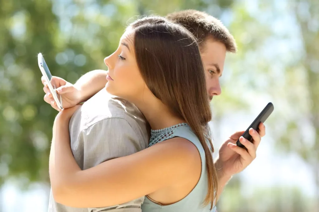 A couple embracing while both are distracted by their phones, highlighting the impact of social media on relationships.