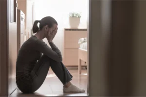 A mom feeling guilt with head in her hands sitting on the floor.
