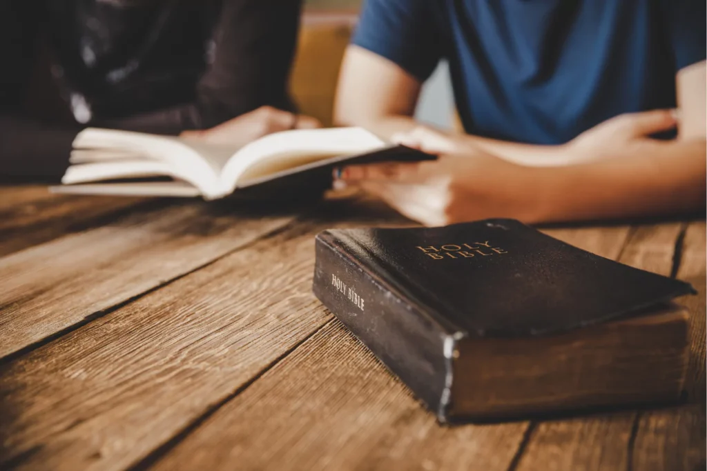 Christian teen with a Bible open on a wood table being discipled by a parent.