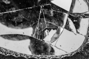 black and white image of a person looking down into a cracked mirror
