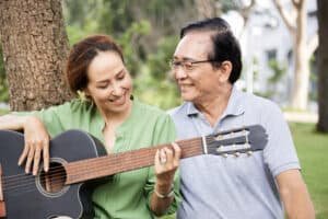 Proud affectionate senior man looking at his talented wife playing guitar and singing when they are resting in park.